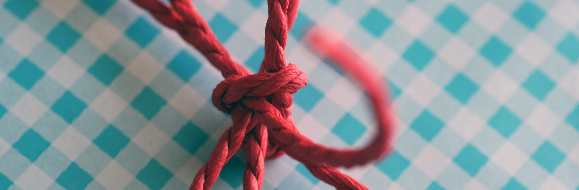 Das Bild zeigt einen roten Knoten vor türkis-weiß-kariertem Hintergrund.